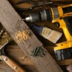 A close-up of various tools including a drill, hammer, and paintbrush on a wooden workbench.