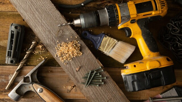 A close-up of various tools including a drill, hammer, and paintbrush on a wooden workbench.